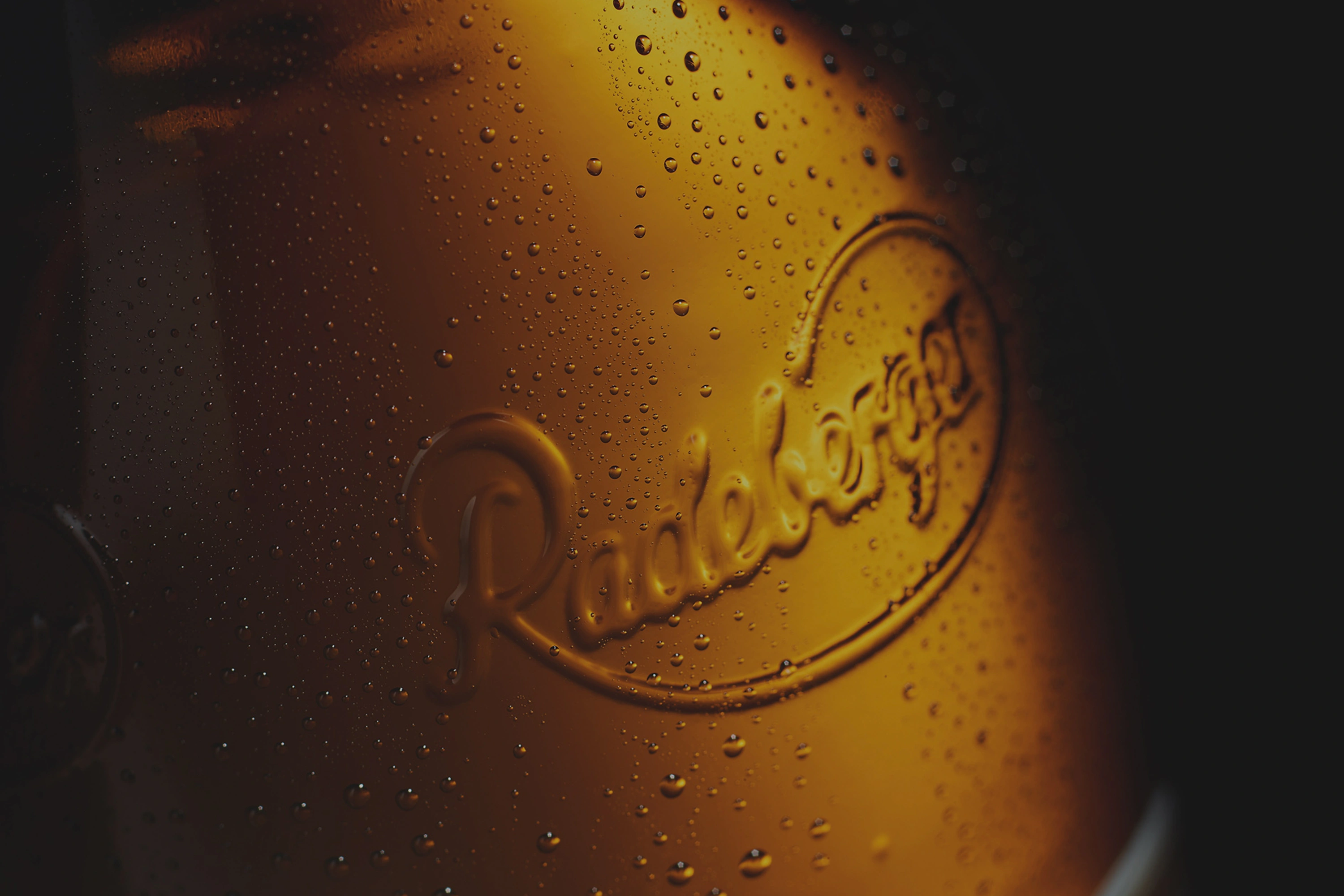 Goldfarbene Fläche mit geprägtem Logo und vielen Wassertropfen.