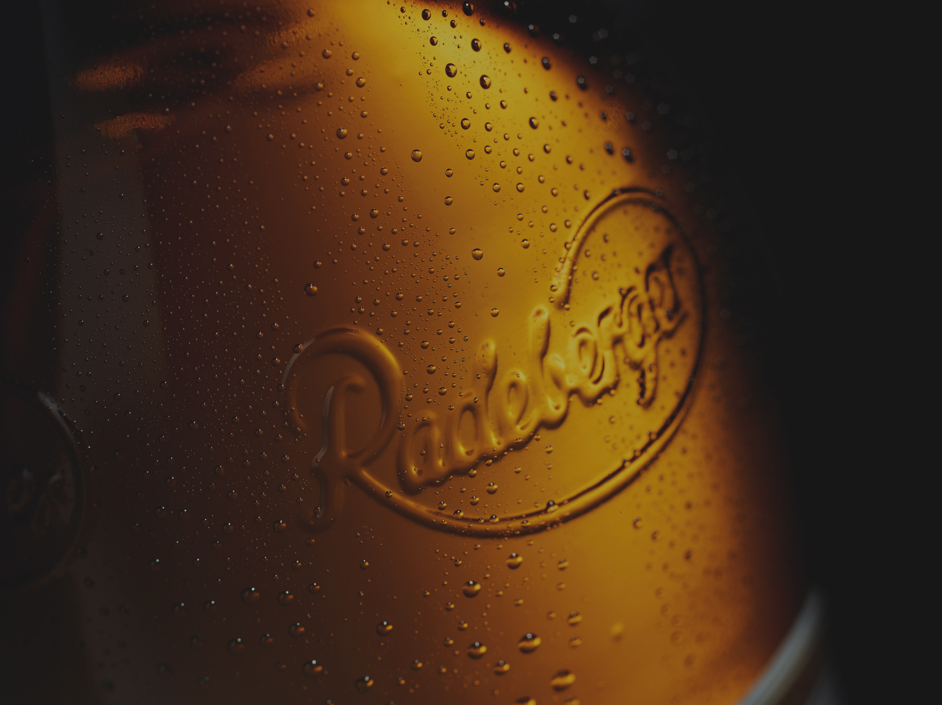 Goldfarbene Fläche mit geprägtem Logo und vielen Wassertropfen.