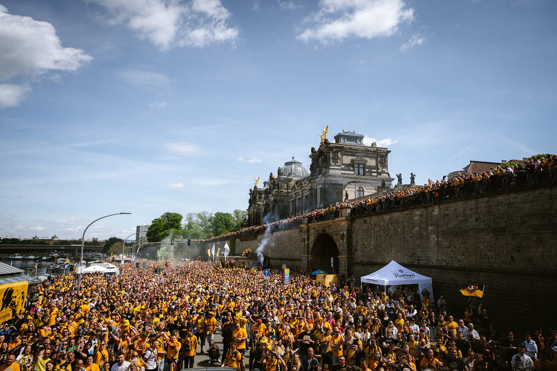 Eine Menschenmenge in gelben Shirts versammelt sich vor einem historischen Gebäude.