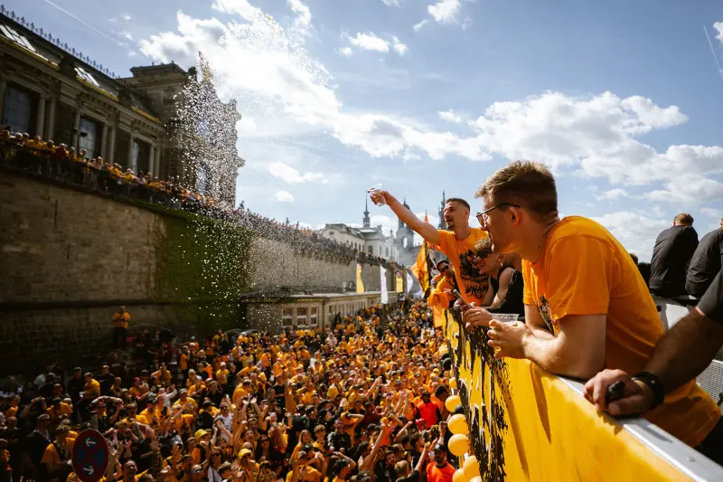 Mehrere Personen in gelben Shirts feiern auf einer Straße, Wasser wird verspritzt.