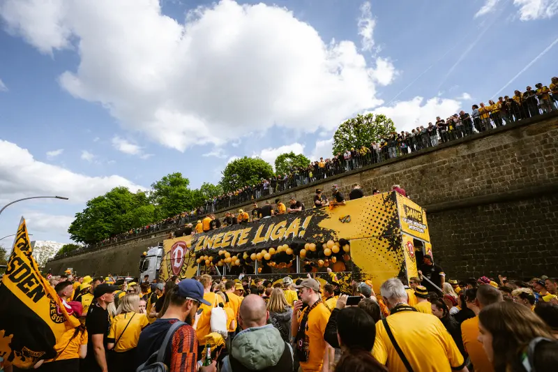 Viele Menschen in gelben Kleidern feiern ausgelassen bei einer Sportveranstaltung im Freien.