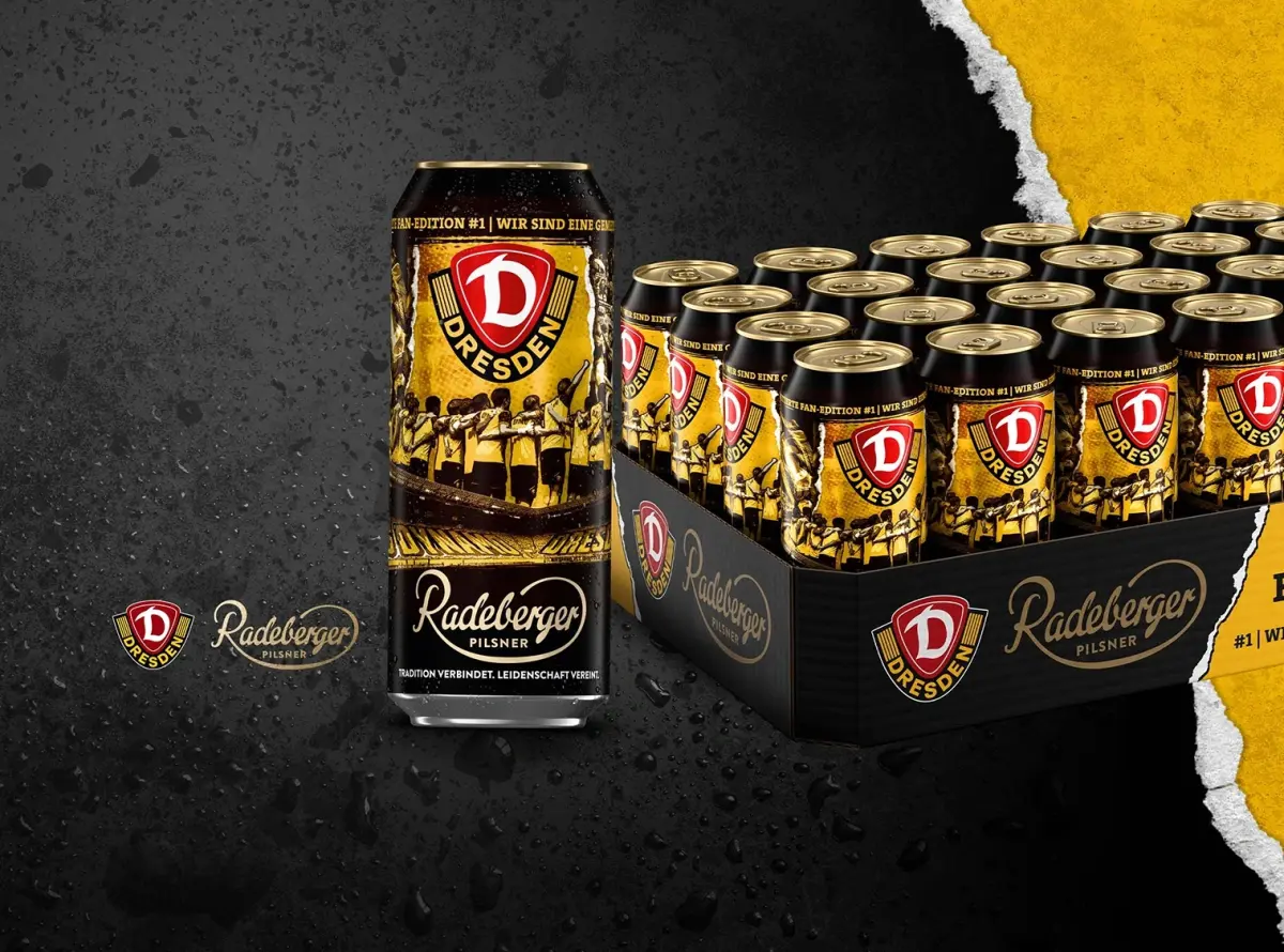 Mehrere Bierdosen im Dynamo-Dresden-Design inklusive Tray vor nassem Hintergrund.