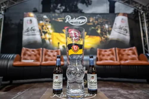 Ein Glas mit Dynamo Dresden und Radeberger Logo steht zwischen zwei Radeberger Bierflaschen auf einem Tisch.