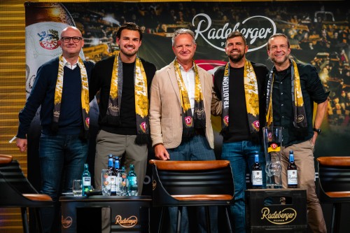 Fünfi Männer stehen auf einer Bühne vor großem Banner von Dynamo Dresden und Radeberger.