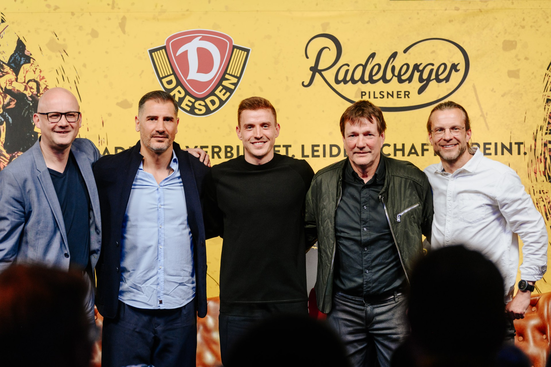 5 Männer stehen nebeneinander auf einer Bühne, hinter ihnen die Logos von Dynamo Dresden und Radeberger Pilsner.