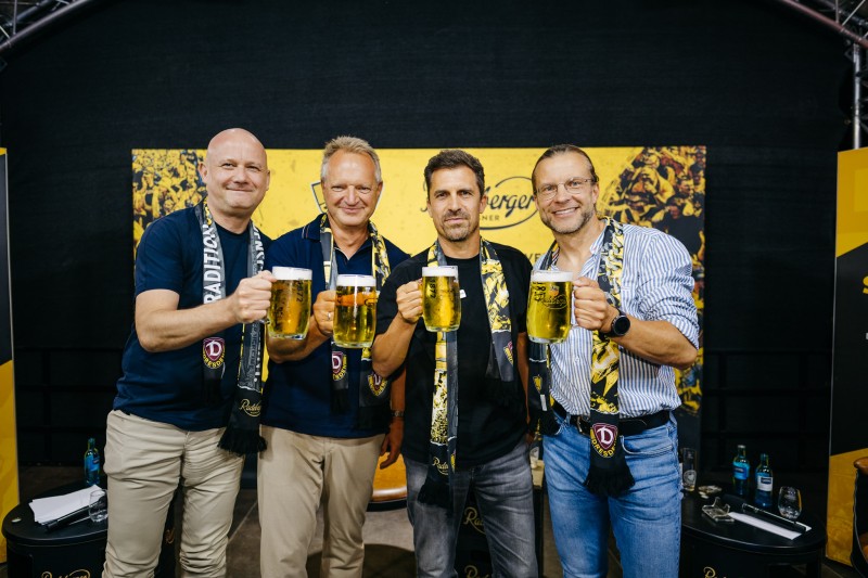 Gruppe von vier Männern mit Radeberger Bierkrügen in der Hand und Dynamo Dresden Schals um den Hals.
