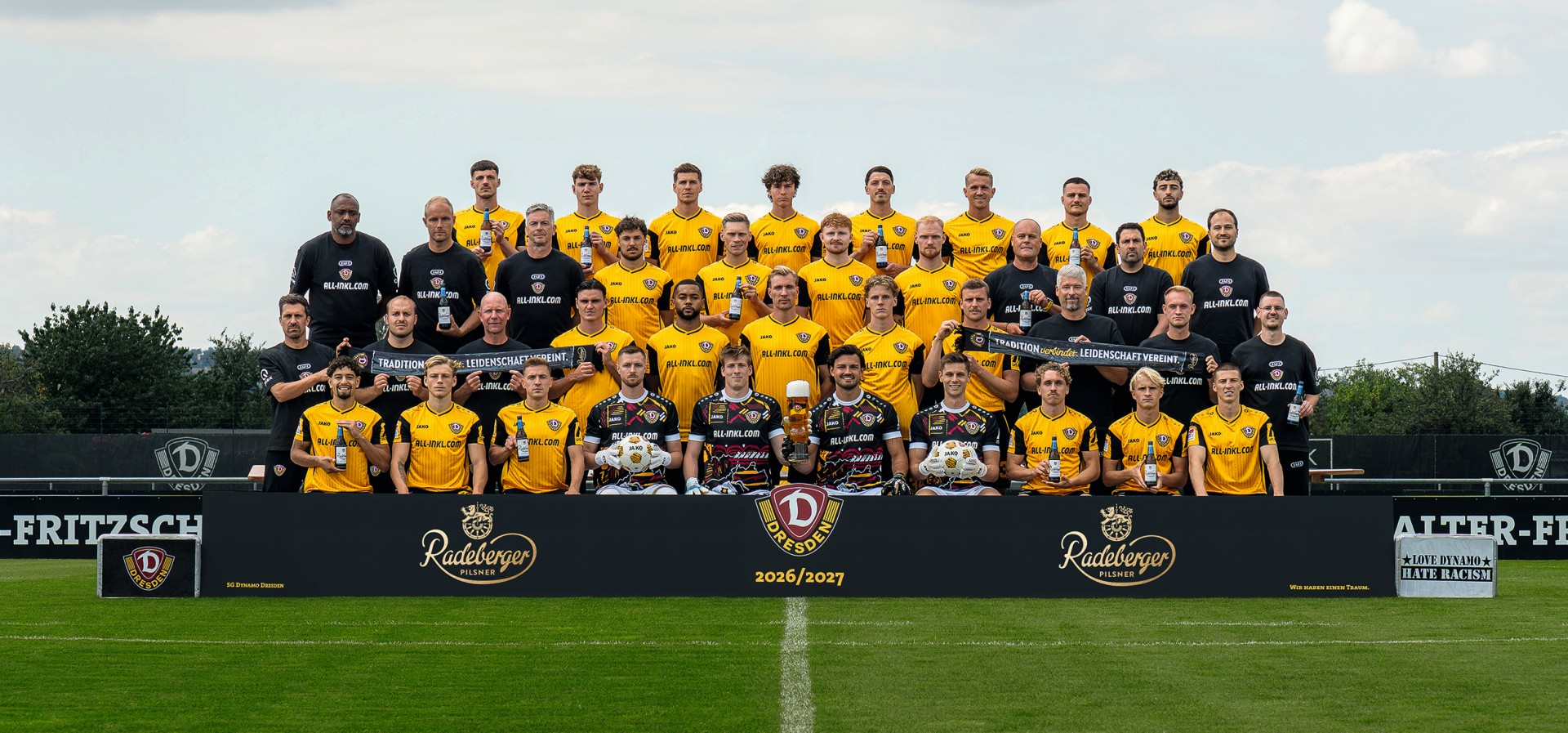 Gruppenbild der Fußballmannschaft Dynamo Dresden auf dem Rasen, davor ein Banner mit dem Vereins- und dem Radeberger Logo.