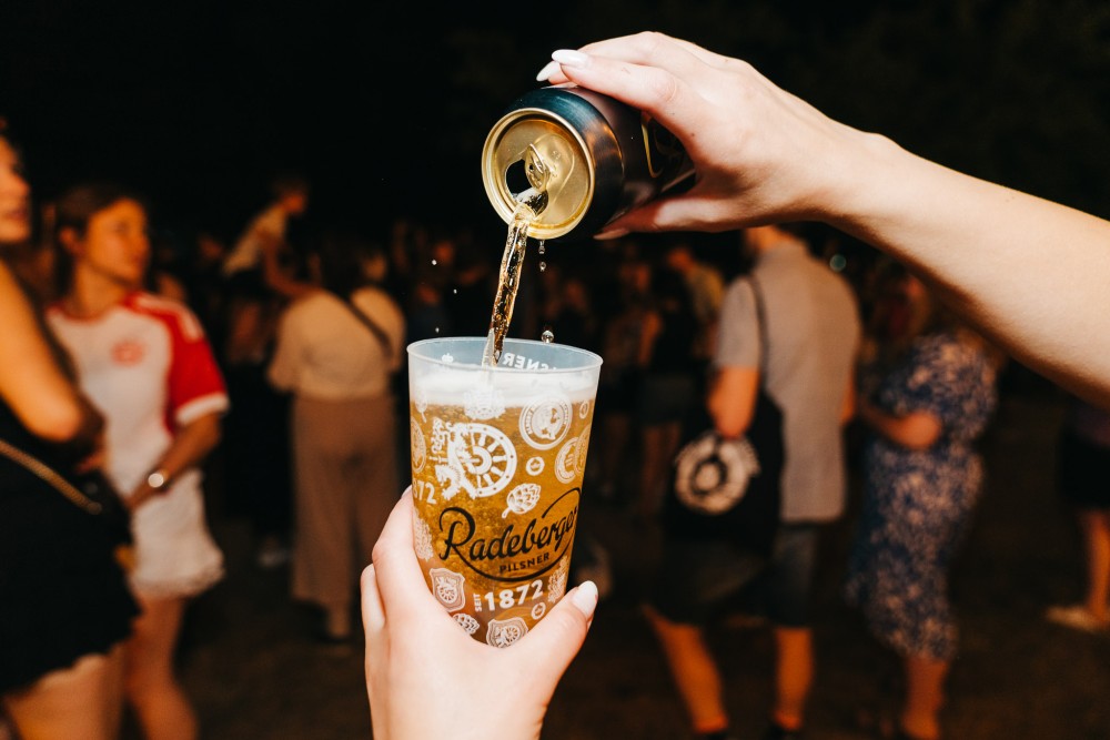 Radeberger Pilsner wird in einen Becher eingeschenkt, im Hintergrund sind Menschen.