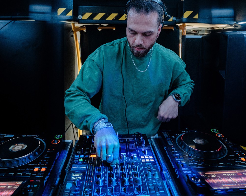 DJ an den Turntables, konzentriert beim Auflegen, blaue Lichteffekte.