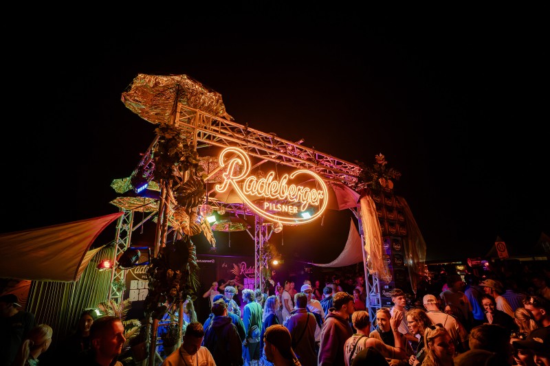 Menschenmenge feiert vor beleuchtetem Radeberger-Pilsner-Stand bei Nacht.