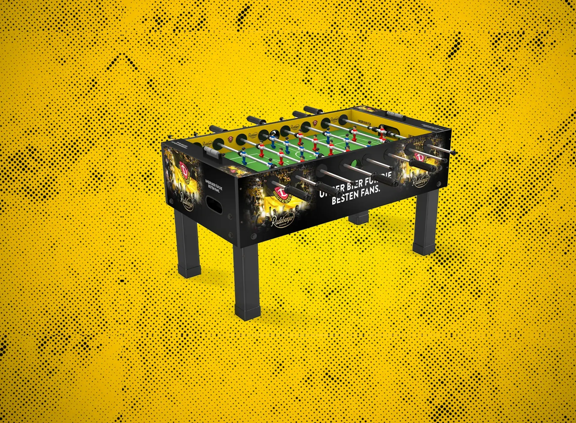 Tischkicker mit Dynamo-Dresden-Design und Spielfiguren auf grünem Spielfeld. Hintergrund in Gelb mit schwarzem Punktmuster.