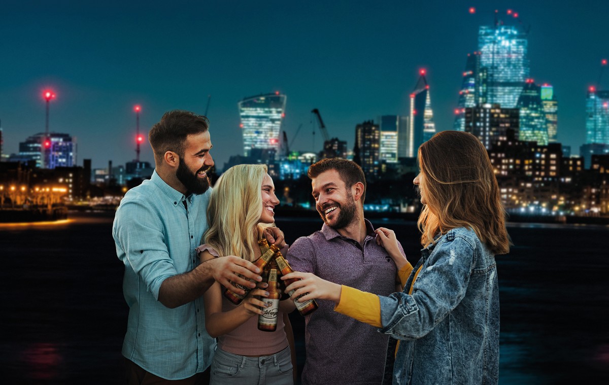 Vier Personen stehen vor einer beleuchteten Skyline und stoßen mit Radeberger Pilsner an.