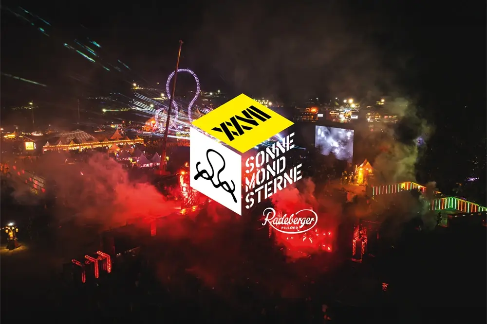 Nachtansicht eines belebten Festivals mit bunten Lichtern und Nebel.