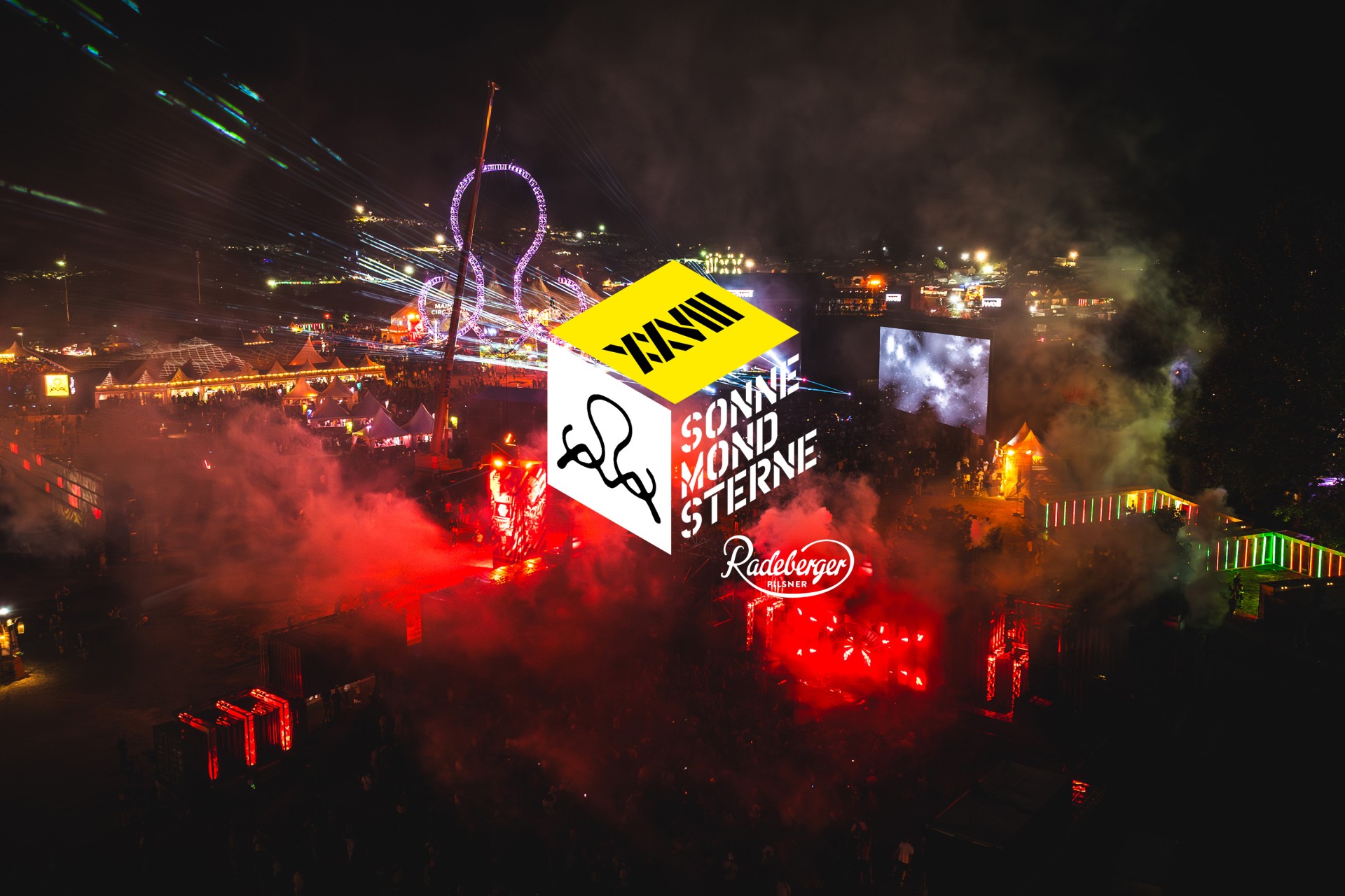 Nachtansicht eines belebten Festivals mit bunten Lichtern und Nebel.