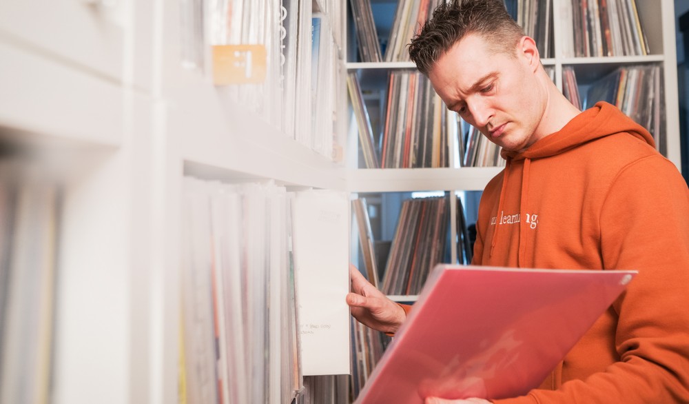 Ein Mann in einem orangefarbenen Kapuzenpullover sucht konzentriert in einem Plattenladen nach Musikalben.