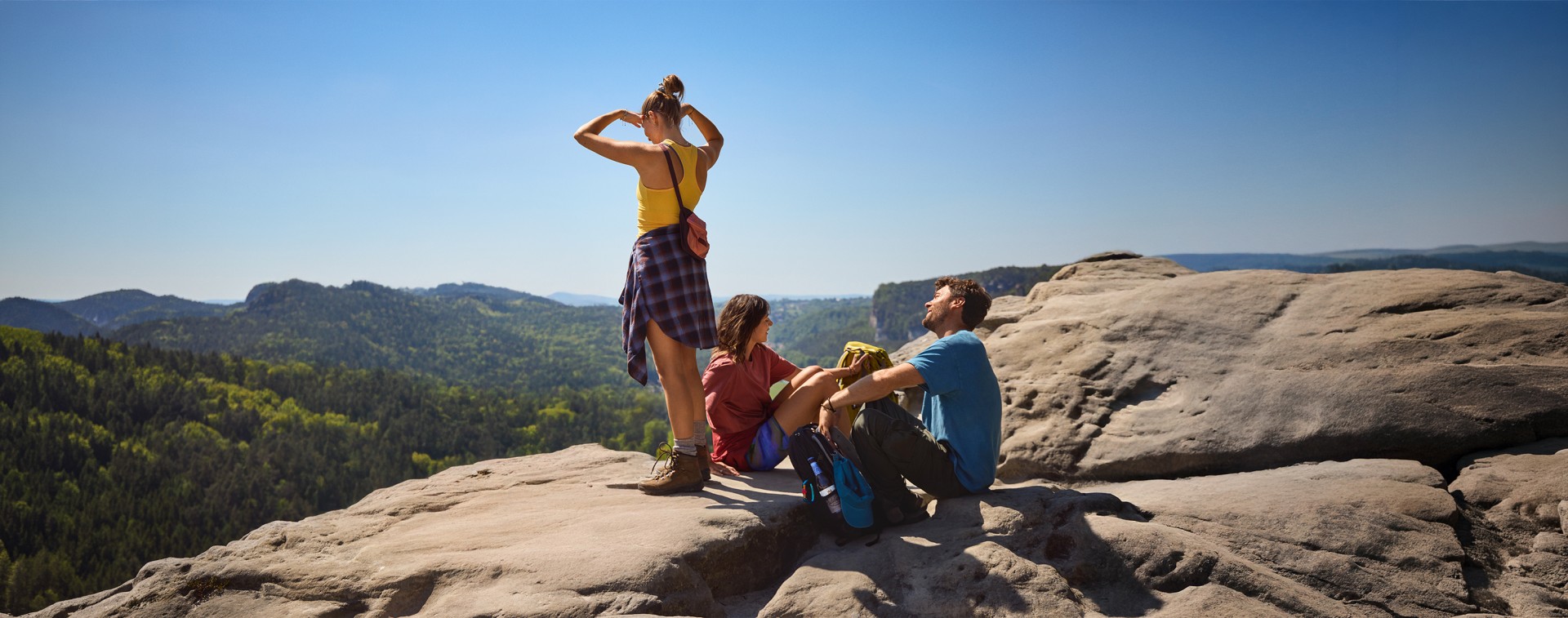 Eine Gruppe von Menschen sitzt auf einer Felsformation, im Hintergrund die Berge der Sächsischen Schweiz.
