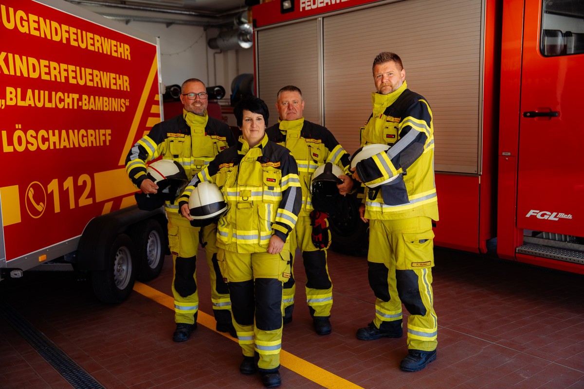 4 Feuerwehrleute stehen vor einen Fahrzeug und einem Anhänger in der Fahrzeughalle.