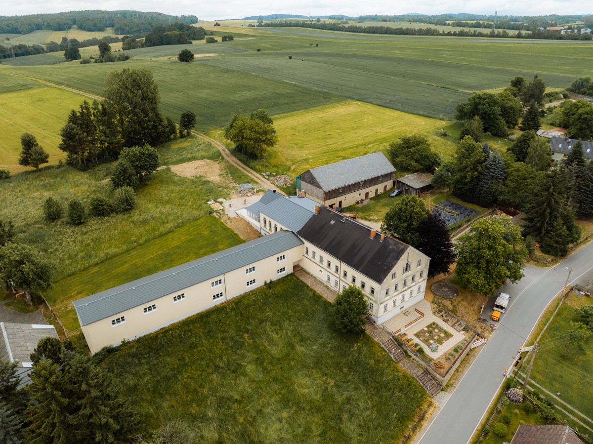Vogelperspektive eines Gebäudes umgeben von Feldern, am rechten Bildrand eine Straße.
