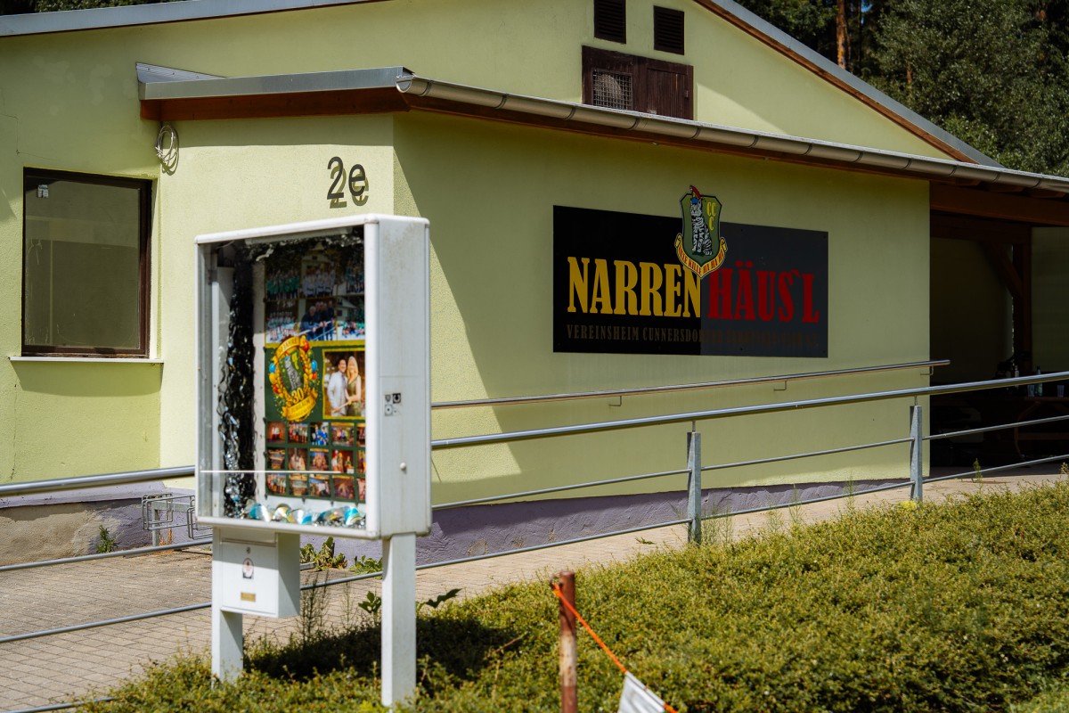 Ein gelbes Gebäude mit der Aufschrift Narrenhäusl. Davor ein Schaukasten mit Bildern.