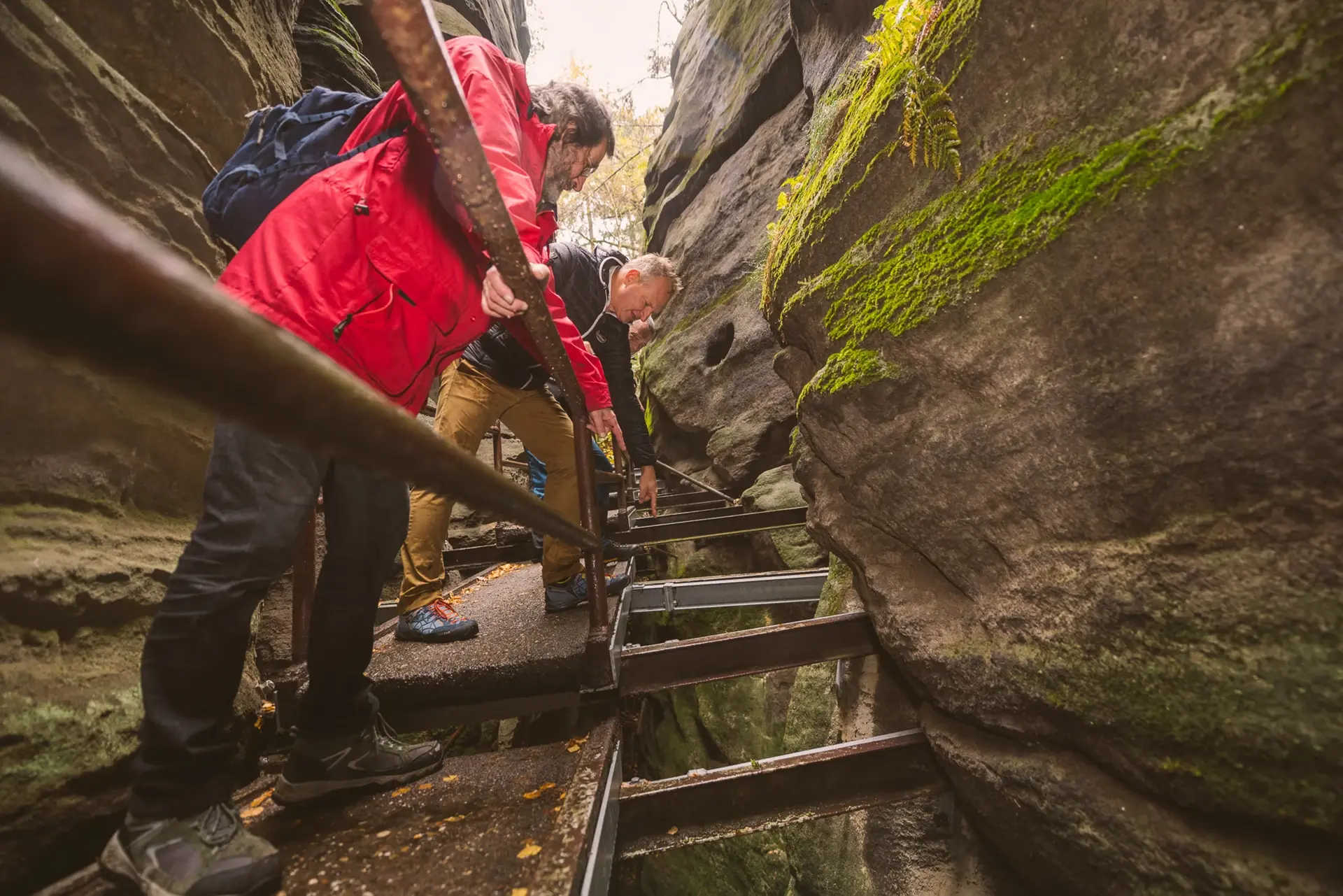 Drei Personen klettern in einer engen Schlucht über Metallstufen nach oben.
