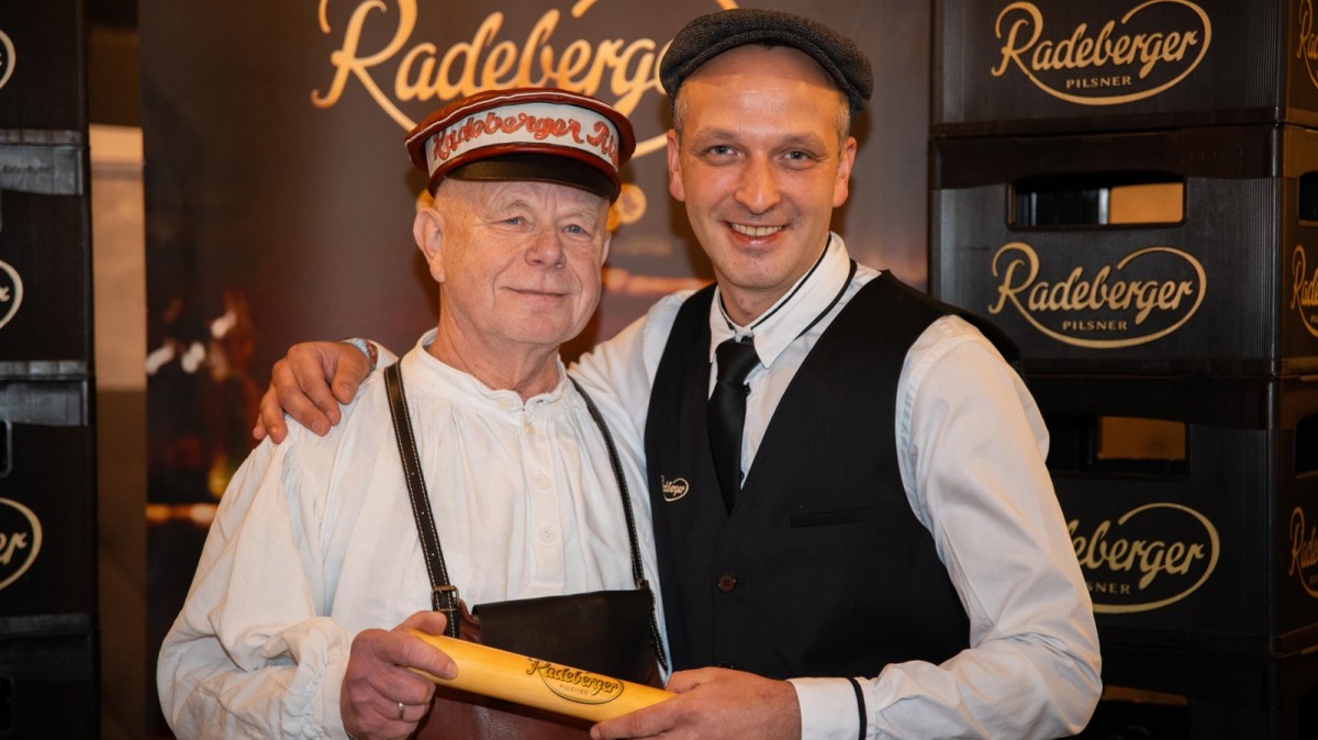 Zwei Männer in traditioneller Kleidung stehen lächelnd nebeneinander.