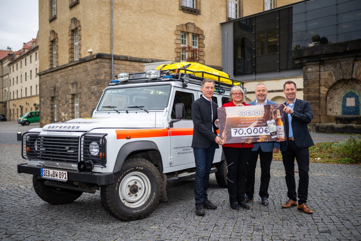 Vier Personen stehen vor einem Geländewagen und halten einen Scheck über 70.000 Euro.