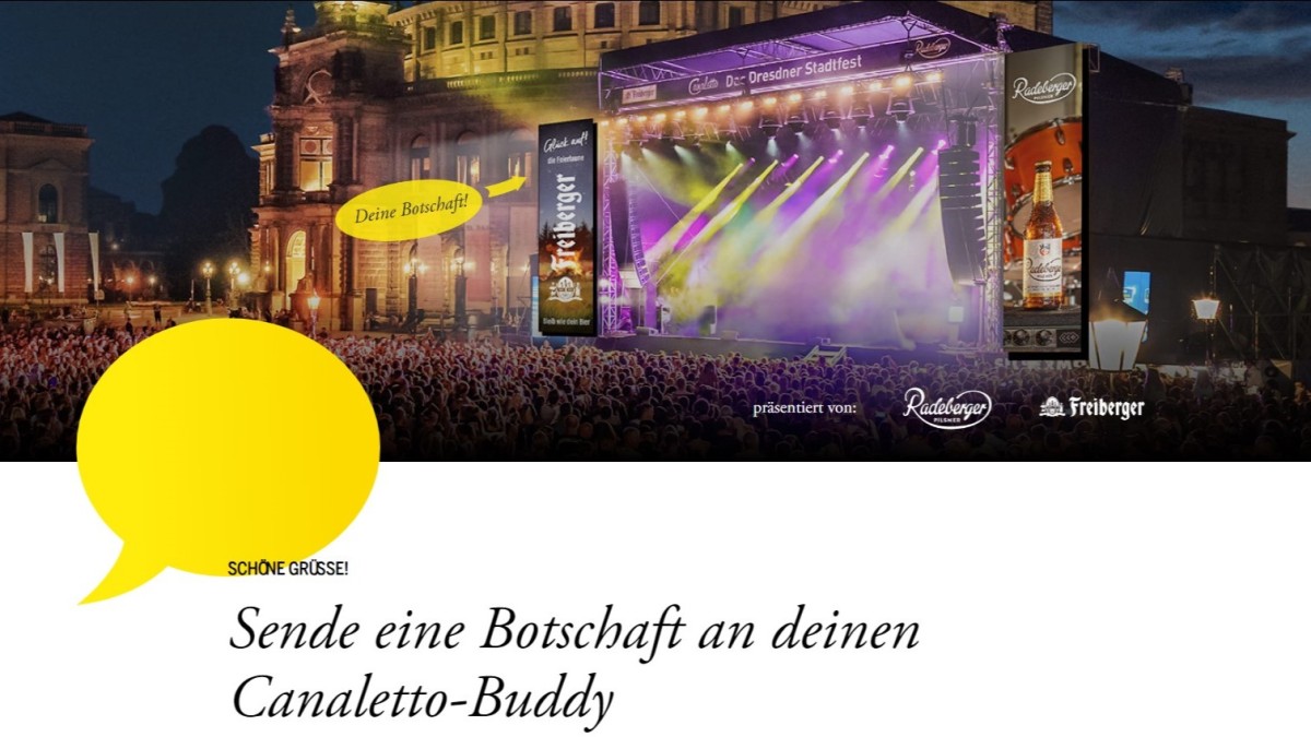 Eine belebte Menschenmenge genießt ein Nachtkonzert vor einer beleuchteten Bühne, umgeben von historischen Gebäuden.