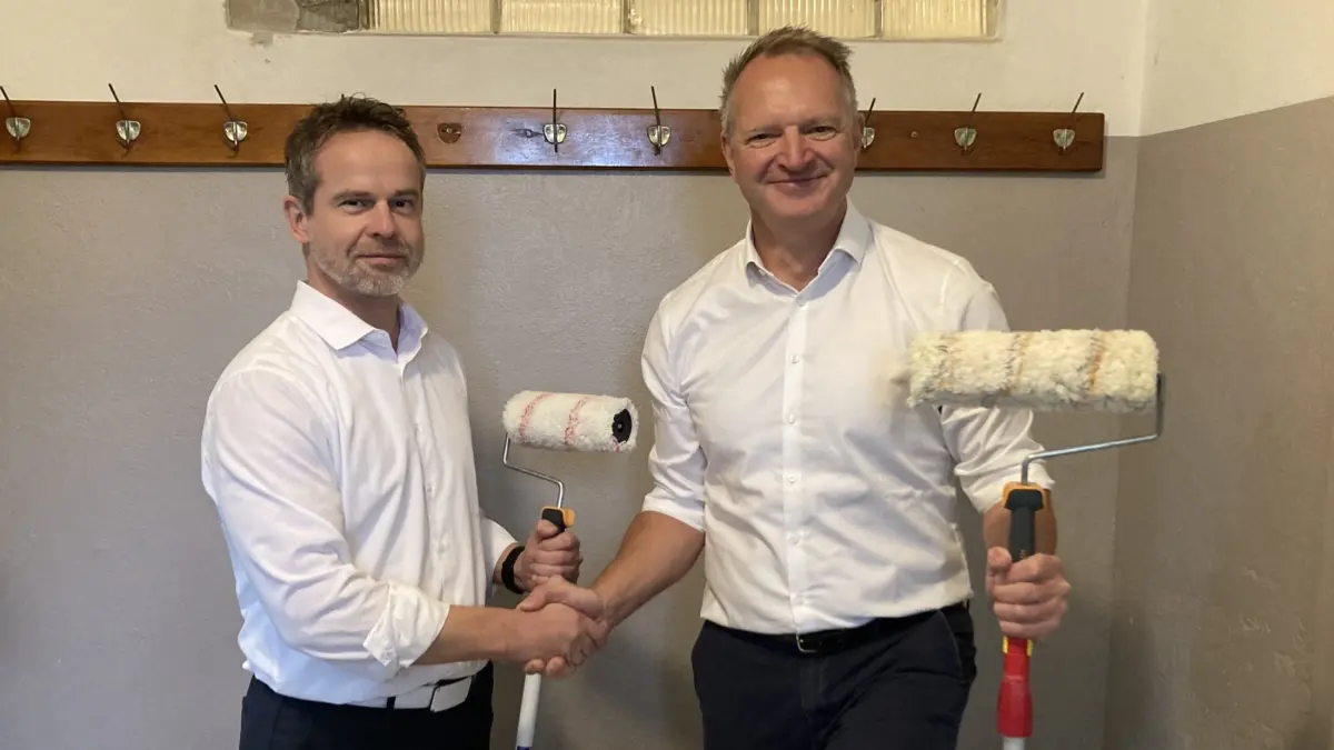 Zwei Männer in Hemden schütteln die Hände und halten Farbroller.