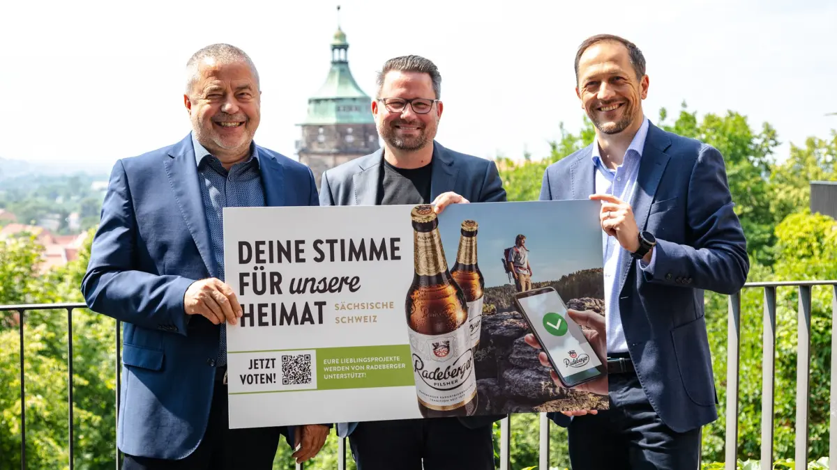 Drei Männer im Anzug halten ein Werbeplakat der Radeberger Heimataktion in die Kamera.