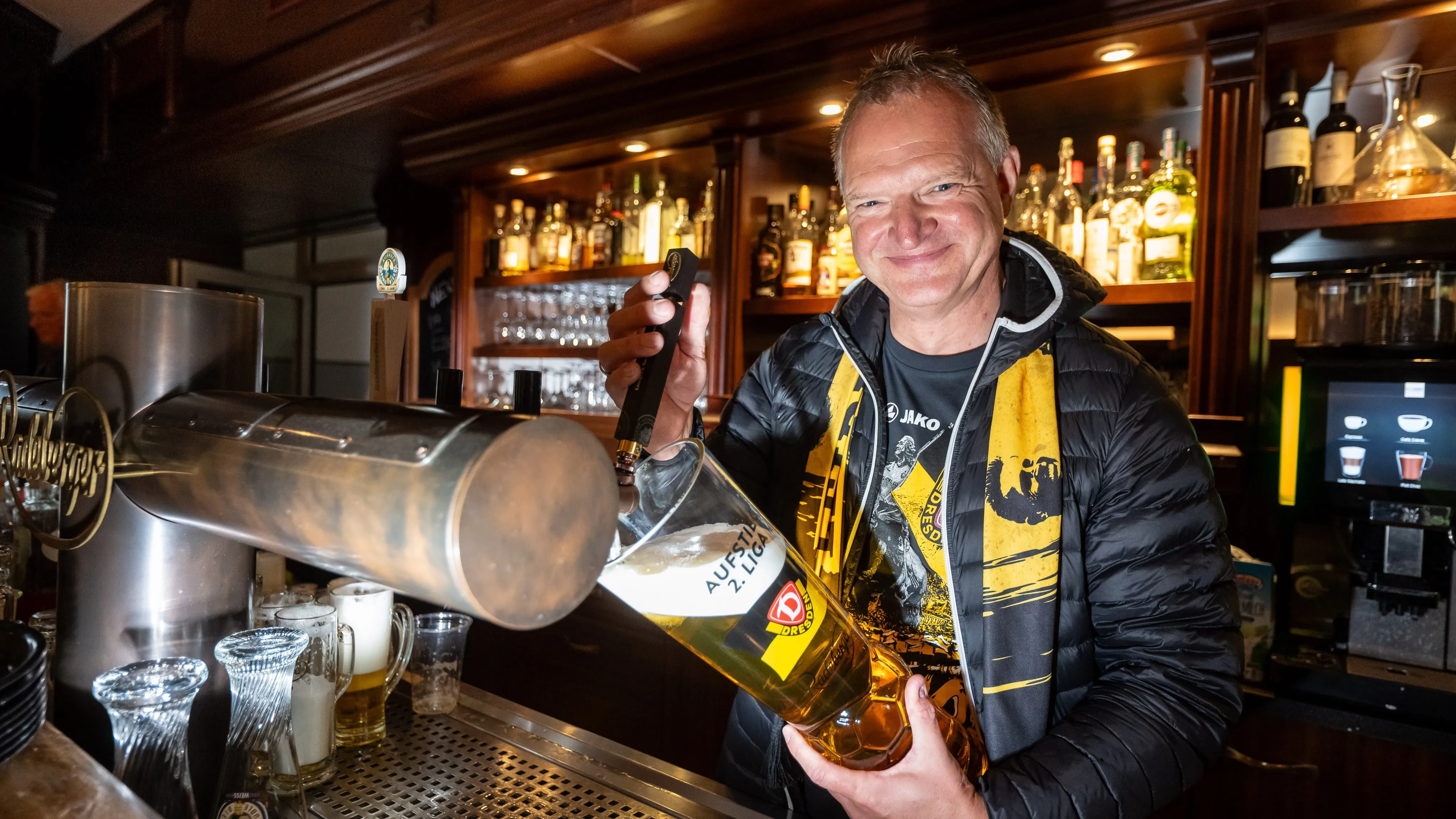 Ein lächelnder Mann schenkt Bier aus einem großen Fass in ein Glas.