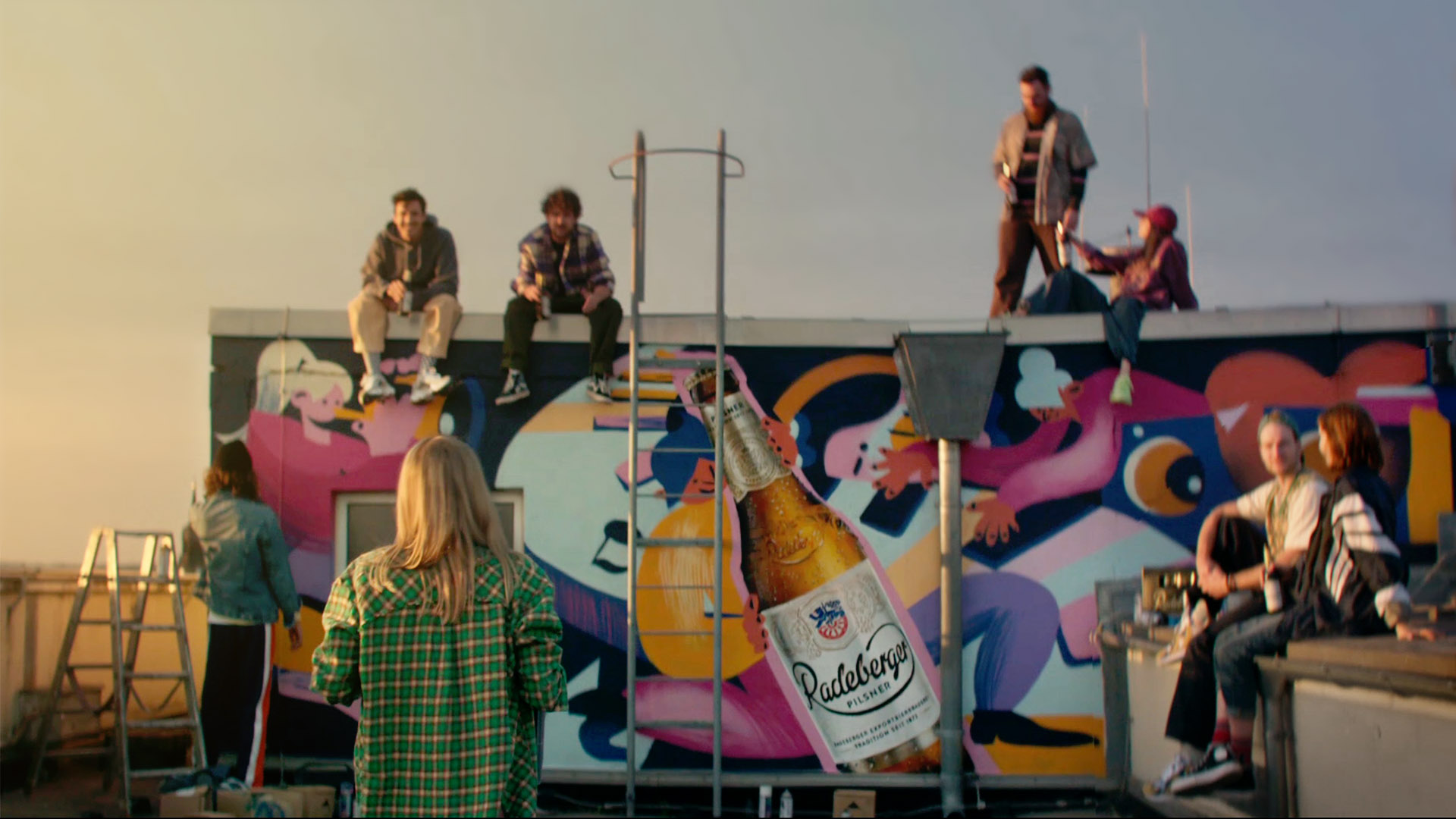 Verschiedene Personen auf einem Dach, im Hintergrund eine besprühte Wand mit Graffiti